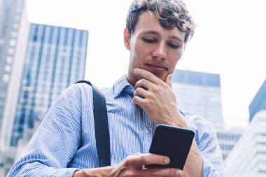 Düşünceli genç adam internetin açık havada sörf yapmak için 4G kablosuz bağlantısıyla finansal haberleri kontrol ediyor. Evrak çantalı beyaz adam ortağından gelen e-postayı inceliyor.