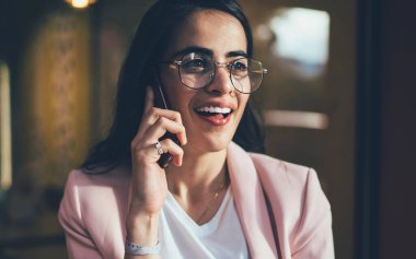 Cep telefonuyla iletişim kurarken gülümseyen klasik gözlüklü pozitif kadın. 20 'li yaşlarda mutlu bir Gürcü kadın açık havada telefonla uluslararası internet kullanıyor.