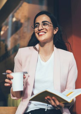 Görme düzeltmesi için optik gözlük takan neşeli kadın gazeteci öğrenme ve sınav hazırlıklarına zaman ayırmak için eğitim kitabıyla gülümseyen ve kafeinli mutlu Gürcü kadın.