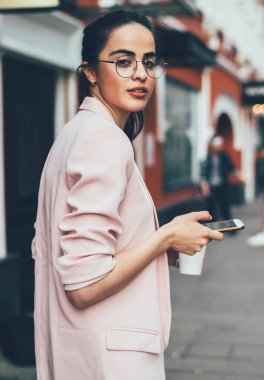 Çekici İspanyol kadın blog yazarının yarı boy portresi cep telefonu aygıtıyla uluslararası şehri keşfetmek için kameraya bakıyor, modern teknoloji kavramı ve çevrimiçi telefon.