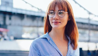 Gözlüklü çekici kızıl saçlı hippi kız cep telefonu aletini elinde tutuyor ve boş zamanlarında başka yere bakıyor modern dijital teknolojiye sahip güzel bir kadın.