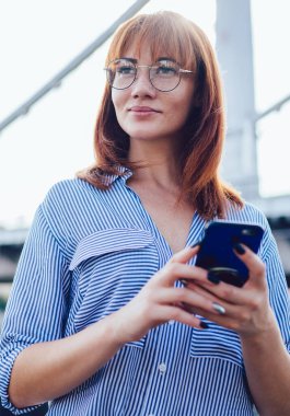 Modern cep telefonunu elinde tutan güzel bir yenilikçi kız sosyal ağda yeni bir yayın fikri, teknoloji ve iletişim kavramını düşünürken kafasını çeviriyor.