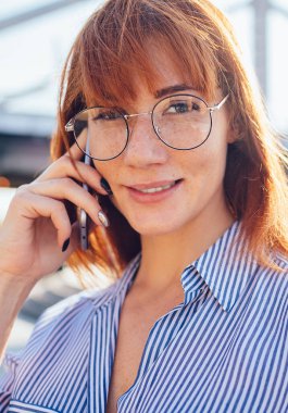 Yüzünde sevimli bir gülümseme olan genç bir kadının yakın plan portresi kameraya bakıyor akıllı telefonu kurutuyor arkadaşıyla konuşuyor, çekici bir kadın milenyumu cep telefonuyla telefonla konuşuyor.
