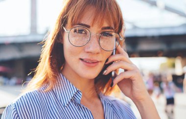 Optik göz giyimi danışmanlığı yapan çekici genç kadının portresi cep telefonu cihazları için gezinme bağlantısı hakkında operatörle yakın çekimde, Beyaz çağda kameraya bakarak ve iletişim kurarak