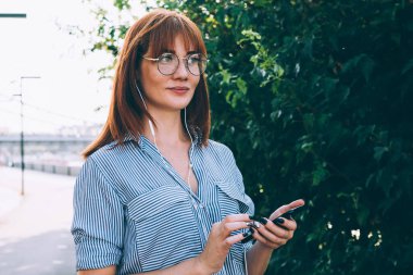 Güneşli bir günde, açık havada cep telefonuyla gezen göz elbiseli çekici kızıl saçlı bir kadın. Aksesuar, güzel bir yeniyetme kız. Cep telefonundan sesli mesajları dinlemeyi seçiyor.