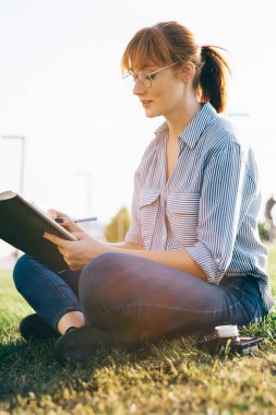 İlkbahar parkında hobi olsun diye resim çizen yaratıcı kadın ressamın yan görünüşü, eğitim için ders kitabına fikirler yazan yetenekli kadın yazar.