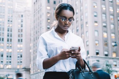Gözlüklü ve resmi kıyafetli şık bir ofis çalışanı, şehir caddesinde cevap vermek için cep telefonunu kullanan meslektaşından mesaj alıyor.