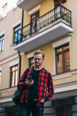 İşaretli kırmızı ve siyah tişörtlü gezginlerden yazın binanın karşısında duran cep telefonunu izliyorlar.