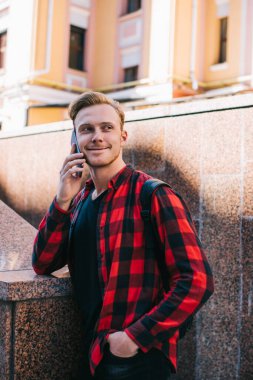 Kırmızı ve siyah tişörtlü neşeli gezgin yazın şehirde gezintiye çıkan cep telefonuyla konuşuyor.