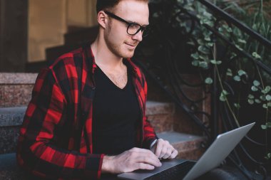 Günlük kıyafet ve gözlük takan, dizüstü bilgisayar kullanan, yeni başlayanlar için fikir arayan, verandada oturan bir yönetici.