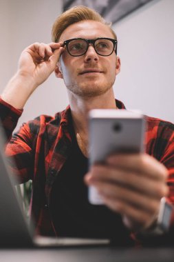 Gündelik genç erkek dizüstü bilgisayar kullanıyor. Yeni başlayan telefonlar üzerinde çalışıyor. Gözlükleri ayarlıyor.