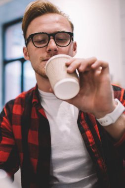Rahat giyinen ve gözlüklü adam işten dinleniyor. Kahve barında oturmuş sıcak içeceğin tadını çıkarıyor.