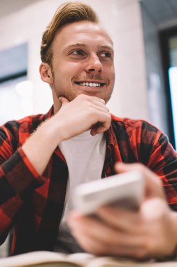 Aşağıdan gülümseyen, düşünceli adam planlama stratejisinden, iş yerinde akıllı telefon kullanırken çenesine yaslanarak başka yöne bakıyor.