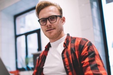 İş yerinde bilgisayarla kameraya bakarken gözlüklü, cep telefonuna dokunan yakışıklı, konsantre bir erkekten.