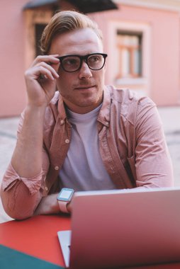 Klasik görüş koruması için gözlüklü, düşünceli hippi bir adam kafeterya masasında oturmuş web sitesi içeriği üzerine kafa yoruyor. Modern dizüstü bilgisayarla uzaktan çalışan dalgın hipster programcı.