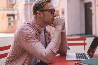 Optik gözlük takan kafası karışmış erkek öğrenci, e-öğrenim için göz koruması sağlıyor ve ders için bilgi hazırlıyor, web sitesi sisteminde düşünceli serbest yazar