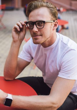 Kendine güveni olan, akıllı saat takan, tablet kullanan, sokak kafesindeki kameraya bakan, kendine güvenen genç bir adam.