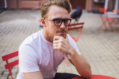 Sosyal ağlar için yayın metni oluştururken kameraya bakarken klasik gözlüklü beyaz erkek blog yazarı portresi, uygulama bağlantısı üzerine düşünen milenyum adamı