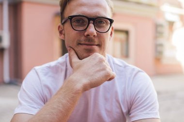 İnternet sosyal ağlarında mesajlaşmak için dijital tablet kullanırken kameraya bakan beyaz erkek blog yazarının portresi, uygulama bağlantısı ve çevrimiçi bilgilendirme üzerine kafa yoran bin yıllık genç adam