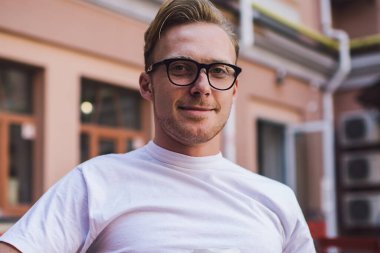 Cafe Terrace 'da arkadaşınızı beklerken kameraya gülümseyen ve kahvenin keyfini çıkaran, klasik gözlüklü mutlu hipster adamın cep telefonu aletini açık havada kullanan pozitiflerin yarım boy portresi.