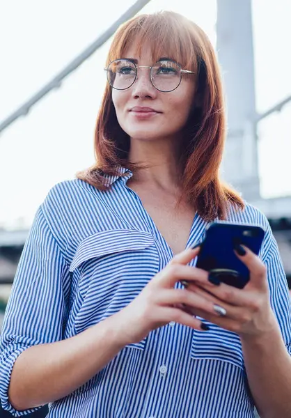 Modern cep telefonunu elinde tutan güzel bir yenilikçi kız sosyal ağda yeni bir yayın fikri, teknoloji ve iletişim kavramını düşünürken kafasını çeviriyor.