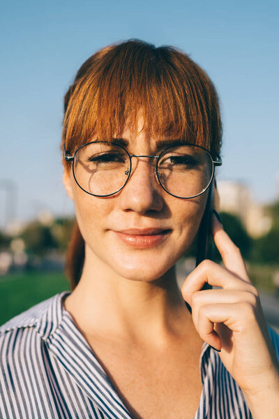 Крупный план портрета привлекательной женщины тысячелетия в классических очках для обеспечения защиты глаз, глядя на камеру во время телефонного звонка с помощью приложения, красивая женщина звонит оператору
