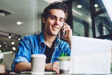 Pozitif yetenekli hippi, akıllı telefon cihazıyla iş arkadaşı ile iletişim kuruyordu. Bilgisayarla masada otururken gülümseyen adam, iyi kablosuz internetin keyfini çıkarıyordu.