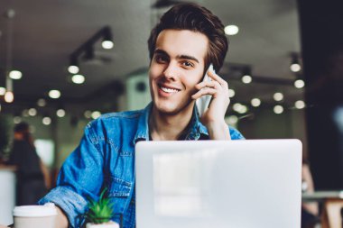 Pozitif neşeli hipster adamın portresi kafenin içinde zaman geçiriyor ve müşteri hizmetlerini ararken kameraya bakıyor yeni dizüstü bilgisayarın güncellemesi hakkında iletişim kurmak için.