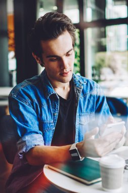 Milenyum hipster çalışanı cep telefonunda iletişim uygulamasını güncellemek ve dizüstü bilgisayar, teknoloji kavramı ve 4G bağlantısı için uzaktan kontrol bildirimi kontrol ediyor.