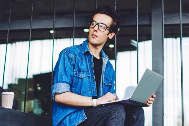 Düşünen hippi çocuk, içerik web sayfasında 4G açık hava interneti kullanarak ciddi makaleler okuduktan sonra aklını yitirdi. Gözlüklü düşünceli adam kampüs merdivenlerinde dizüstü bilgisayarlı cihazlarla vakit geçiriyor.