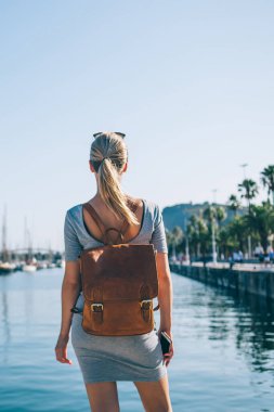 Barselona 'nın deniz kenarında parlak yaz güneşiyle bekleyen gri elbiseli ve deri çantalı sarışının arkası.