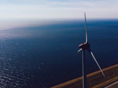 Dönen pervaneli yel değirmeni türbini, sahil şeridi ve tarım arazisi çayırında duruyor. Temiz kaynaklar için yenilenebilir enerji üretiyor. Elektrik enerjisi eko üretimi