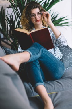 Optik gözlüklü, pozitif zeki hippi kız rahat koltukta uzanmış göz koruması sağlıyor ve boş zamanlarında romantik en çok satanlar kitabıyla keyif çatıyor.