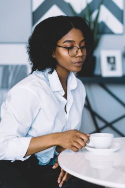 Düşünceli, koyu tenli, optik gözlüklü hippi kız kahve saatinde masada otururken, arkadaşının fotoğraf çekmesini sağlayan gazete dergisinden gelen haberleri okumasını sağlıyor.