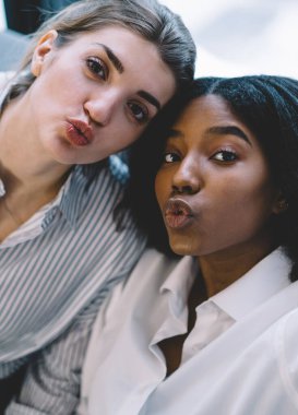 Çekici afro-amerikan ve beyaz kadın arkadaşlarının yakın portresi ördek suratı yapıyor ve birlikte vakit geçirirken kameraya bakıyor evde boş zaman geçiriyor, çok kültürlü insanlar.
