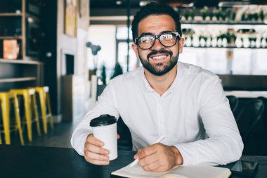 Gözlüklü başarılı bir adamın portresi not defteri için kişisel ders kitabıyla birlikte çalışıyor. Mesafe kontrolü sırasında kameraya gülümseyen ve strateji listesi olan mutlu bir erkek.