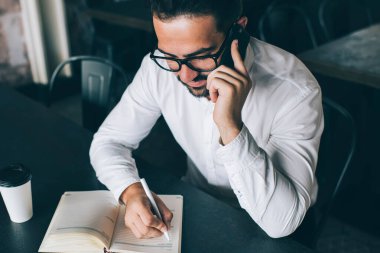 Deneyimli bir erkek tüccar, cep telefonu aygıtı ve internet bağlantısı kullanarak internet üzerinden iletişim kurma kavramını kullanarak proje hakkında bilgi almak için sekreterini arıyor.