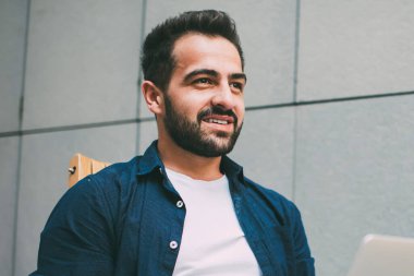 Elinde cep telefonu olan olumlu hipster bir adamın elinde diğer tarafa bakıp gülümserken dizüstü bilgisayar güncellemesi ve serbest çalışma konsepti hakkında danışmanlık için bekleyen programcı bir profesyonelin yan görüntüsü.