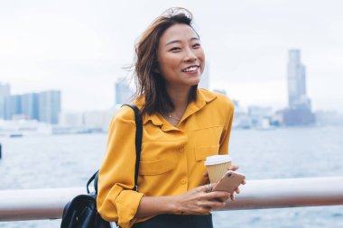 Çin metropolünü keşfetmek için Hong Kong şehir merkezinde bekleyen arkadaşına gülümseyen neşeli bayan öğrencinin yarım boy portresi, dışarıda sevinen pozitif blog yazarı