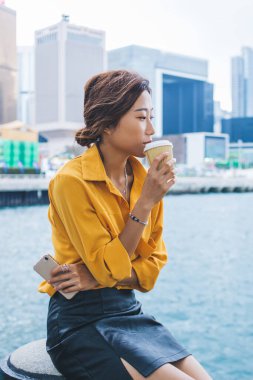 Hong Kong 'un arka planında dinlenirken, tatil boyunca kafa yoran Japon bir kadının dinlenme yerlerinde keyif çattığı yemek fincanından nefis kafein içen dalgın bir bayan turist.