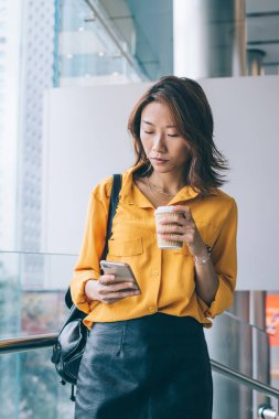 Güzel meşgul Asyalı kadın, gündelik kıyafetleriyle modern dijital akıllı telefonla iletişim kuruyor ve sörf yapıyor.