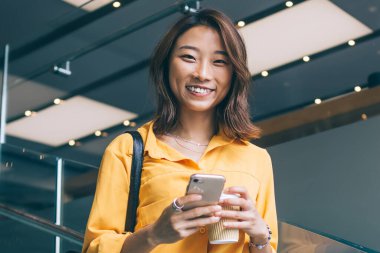 Cep telefonu cihazı olan güzel hippi kızın yarım boy portresi evde durduğu ve neşeli Asyalı bir kadının akıllı telefon aracılığıyla online iletişim sırasında mutluluğu hissettiği için.