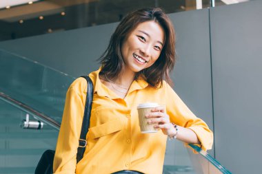 Çekici, mutlu, sarı gömlekli, siyah deri etekli, sırt çantalı, kahve ve cep telefonlu güzel bir Asyalı kadın Hong Kong 'da kapalı kapılar ardında duruyor.