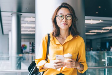 Göz kamaştırıcı gözlüklü çekici kadın blogcunun yarım boy portresi kahve molası sırasında kameraya gülümseyen gözler sağlamak için cep telefonu cihazıyla iletişim kurmak için, milenyum insanı