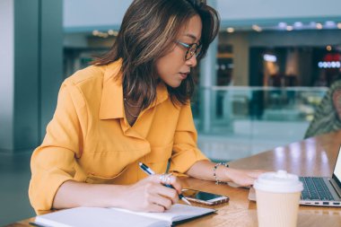 Optik gözlüklü çekici Çinli kız öğrenci, yüksek hızlı internet bağlantısı ile birlikte çalışma alanındaki sınav hazırlıkları sırasında üniversite web sitesinde bilgi arıyor.