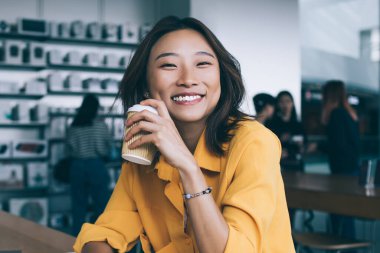 Mutlu Asyalı kadın serbest yazar, yemek arasında laptopunu kapatıp kahve içiyor ve Hong Kong 'daki elektronik mağazasında kameraya bakıyor.