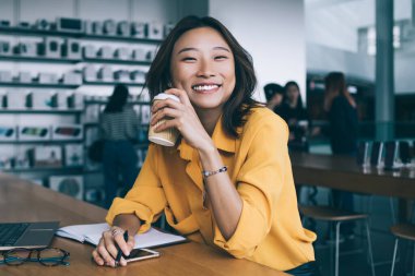 Mutlu Asyalı kadın serbest yazar, yemek arasında laptopunu kapatıp kahve içiyor ve Hong Kong 'daki elektronik mağazasında kameraya bakıyor.