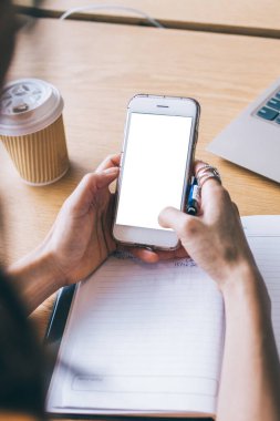 İnce kadın elleri Hong Kong 'da defter ve kahve fincanı ile ahşap masada modern akıllı telefona bakıyor.