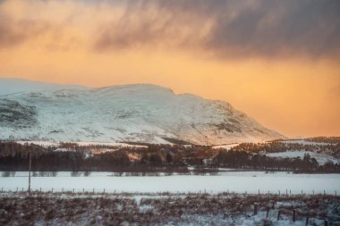 A snow-covered mountain landscape at sunset in Laggan, Scotland clipart