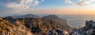 Güney Afrika 'daki Table Dağı' nın tepesinden gün batımında okyanus ve dağların panoramik görüntüsü.